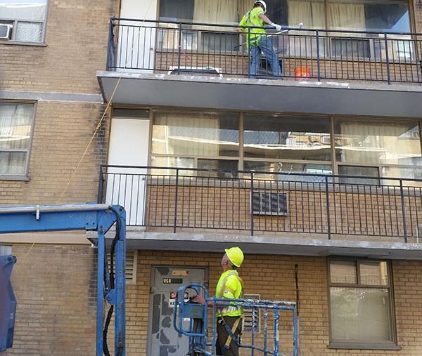 2 werkmannen werken aan gevel van appartement. Reparatie beton van de onderzijde.