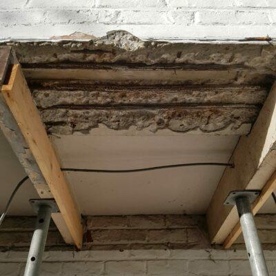Plafond van balkon. Zeer ernstig beschadigd beton. Doorroeste bewapening. Bros beton. Deels uitgekapt. Gestut met steunen.